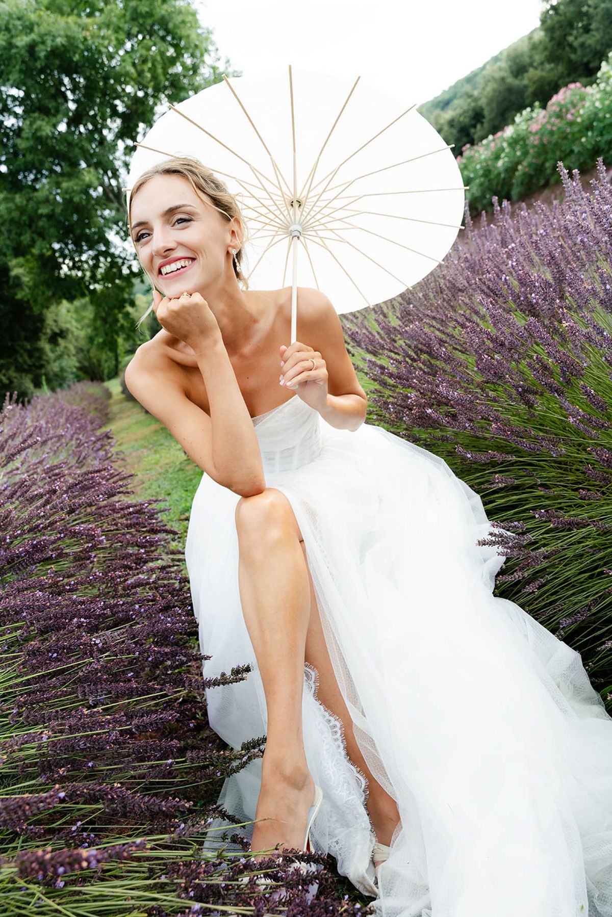 Bride in white gown with parasol seated in lavender field at Domaine de Valbonne