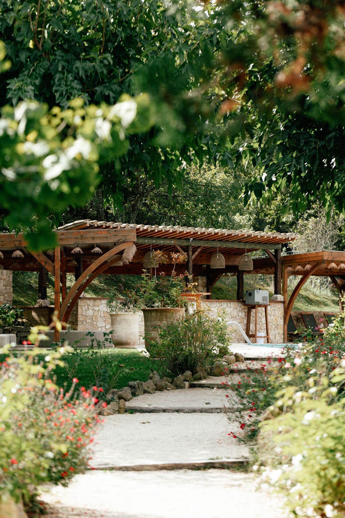 Wooden pergola with pendant lights and poppy-lined path in the gardens at Domaine de Valbonne