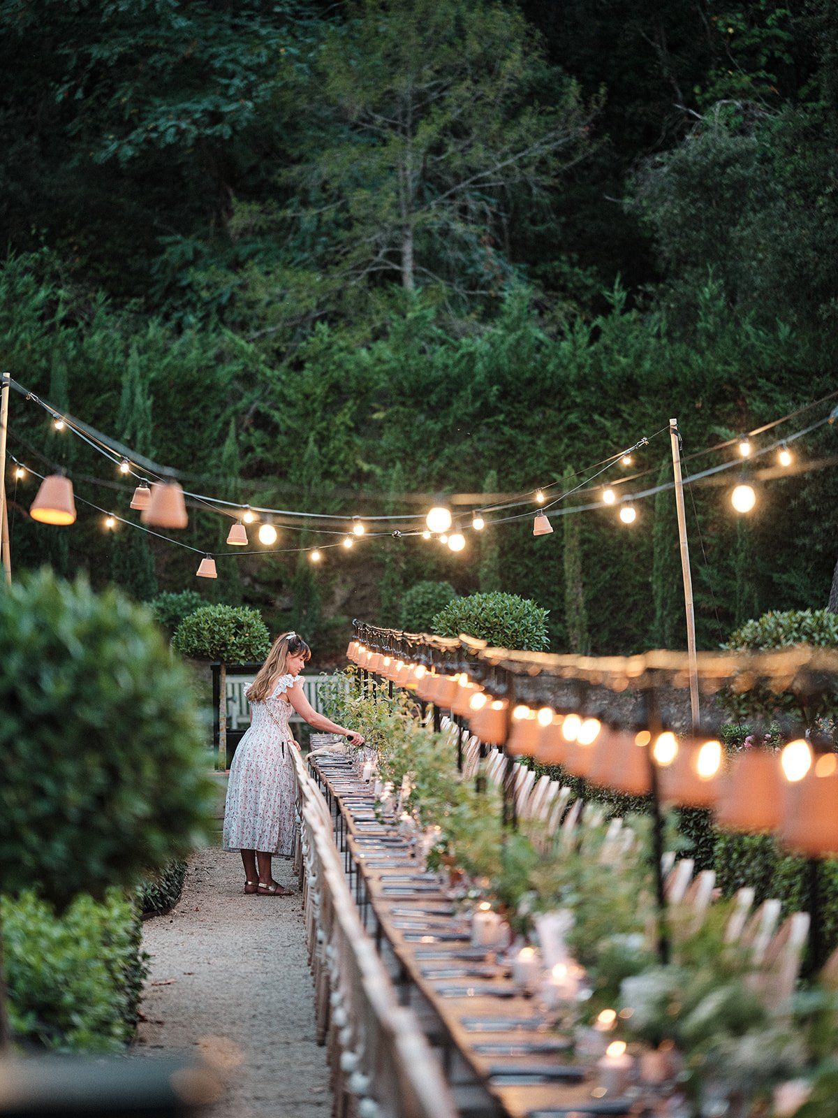 Long dinner table set beneath string lights on the lawn