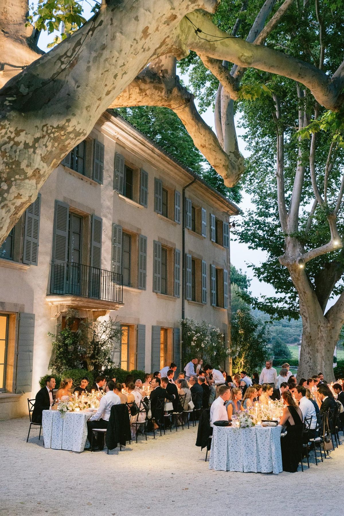 Chateau facade at dusk with guests gathered beneath the trees