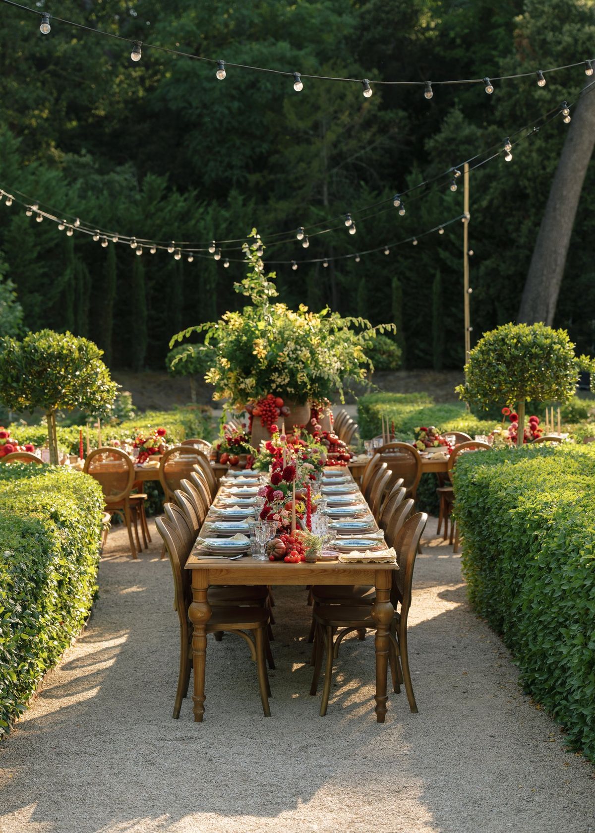 Long dinner table set beneath string lights with a floral centerpiece