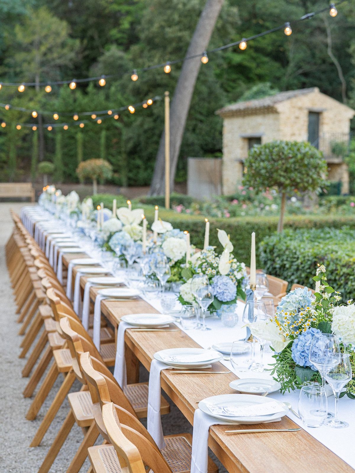 Long dinner table set beneath string lights with the chateau behind