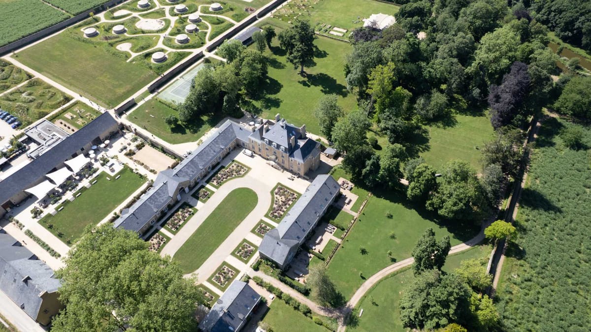 Aerial view of the Domaine Le Mezo estate showing the chateau, courtyard buildings, tennis court and wooded parkland