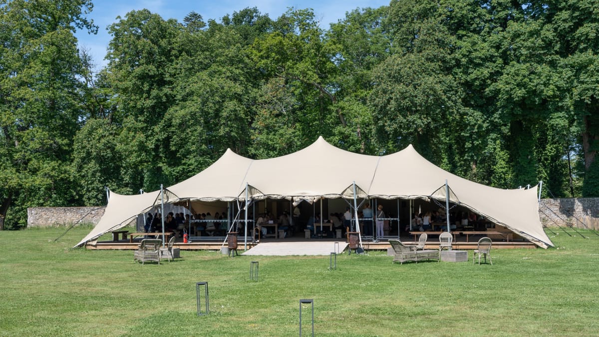 Guests seated at long tables under the stretch tent on the lawn at Domaine Le Mezo