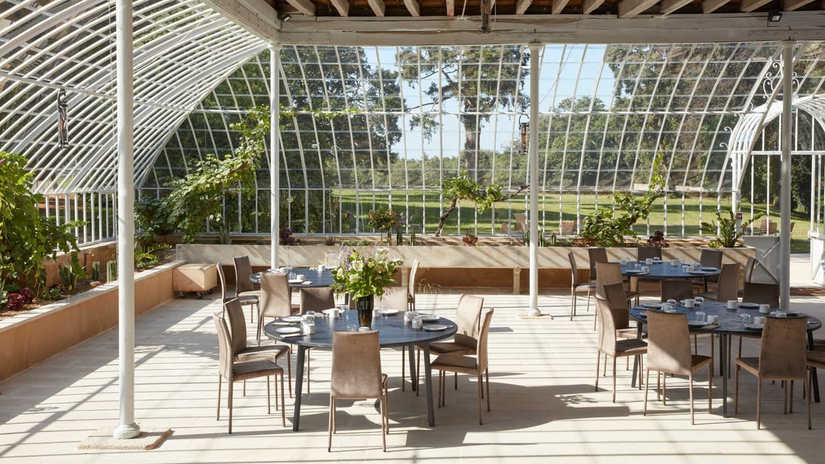 Round tables laid for dinner under the glass roof of the nineteenth century greenhouse at Domaine Le Mezo