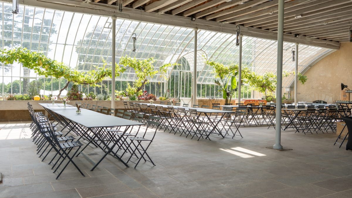 Long tables and folding chairs set out in the greenhouse at Domaine Le Mezo beneath trained vines