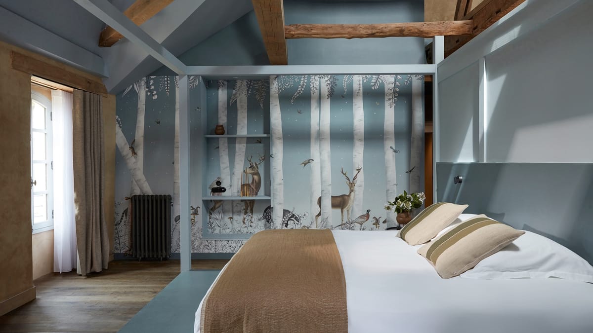 Bedroom at Domaine Le Mezo with a painted woodland mural, exposed beams and a painted timber frame around the bed