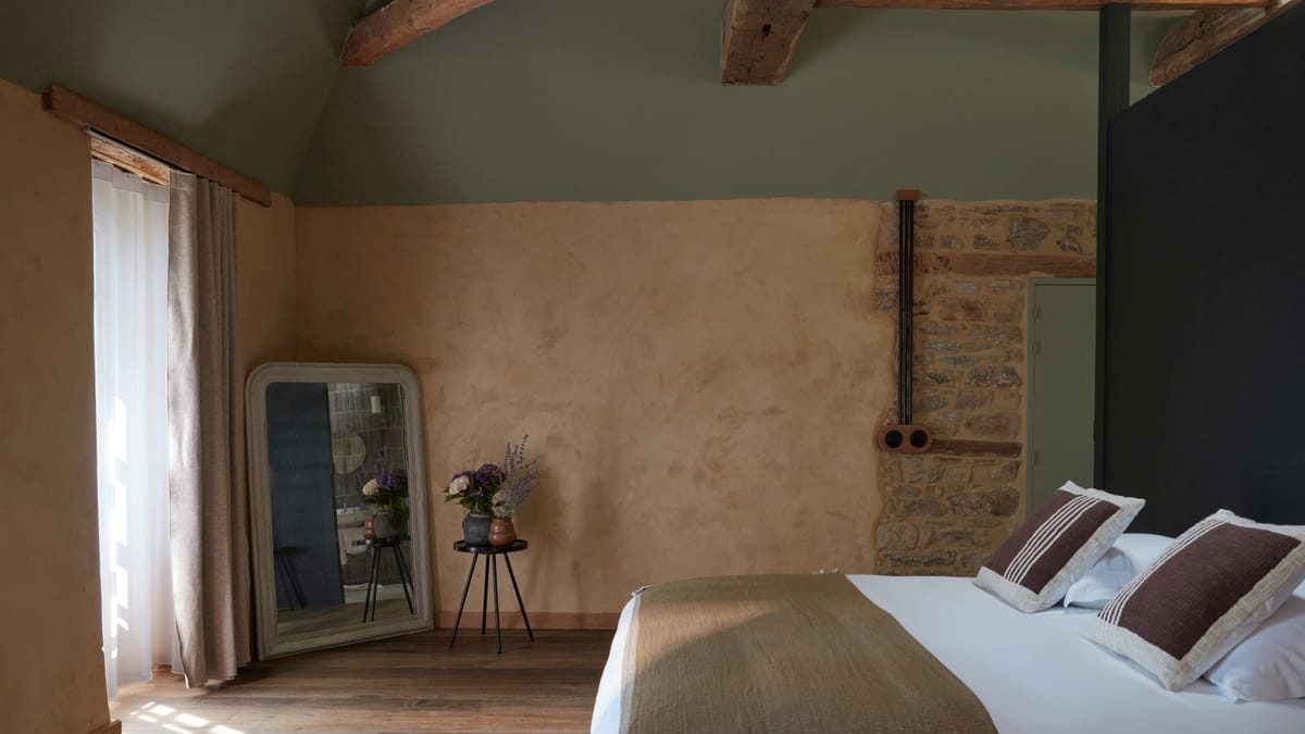 Bedroom at Domaine Le Mezo with lime plaster walls, exposed stone and an arched mirror