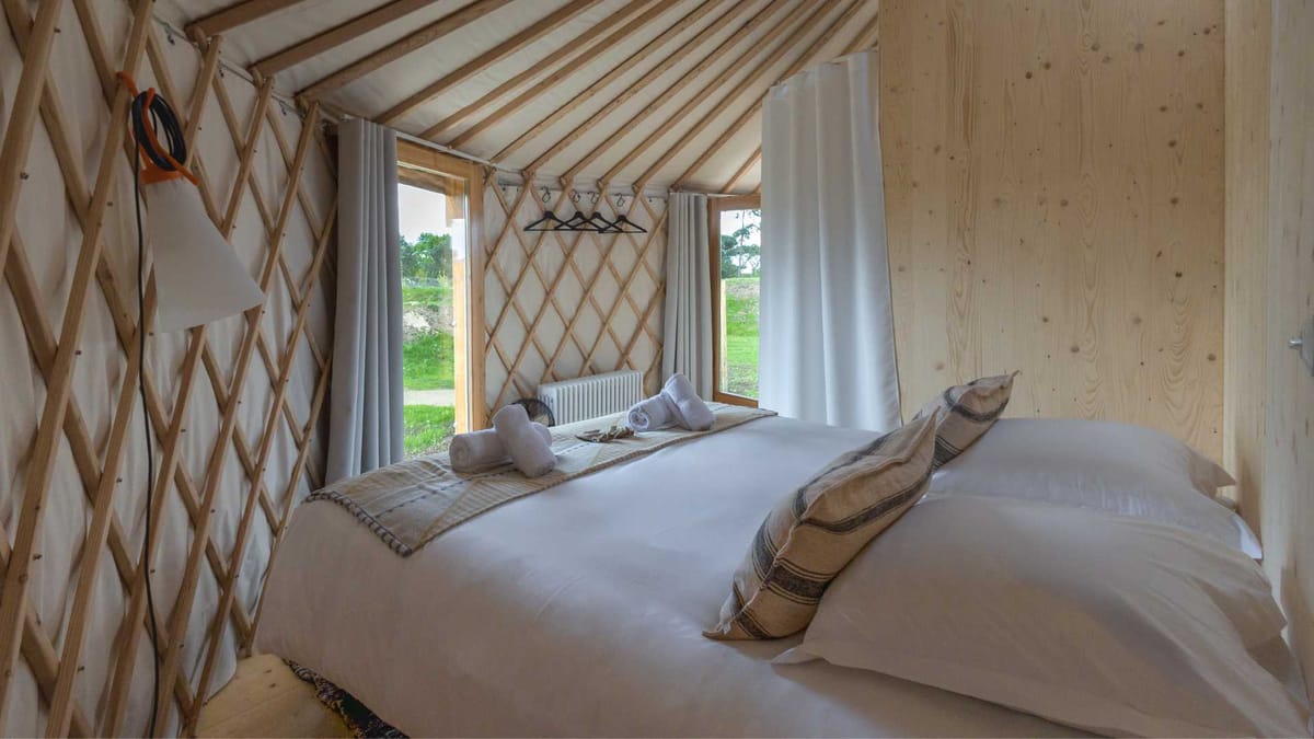 Interior of a yurt at Domaine Le Mezo with a lattice frame, timber wall and made up bed