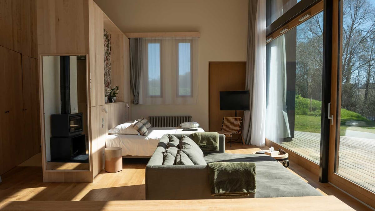 Interior of the eco lodge at Domaine Le Mezo with a wood burner, linen sofa and full height glazing onto the deck
