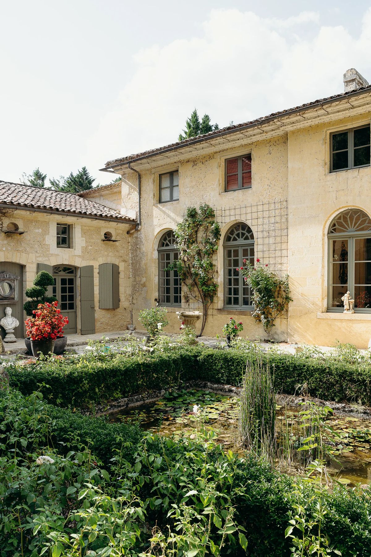The courtyard facade with arched windows and shutters, above a clipped hedge and lily pond