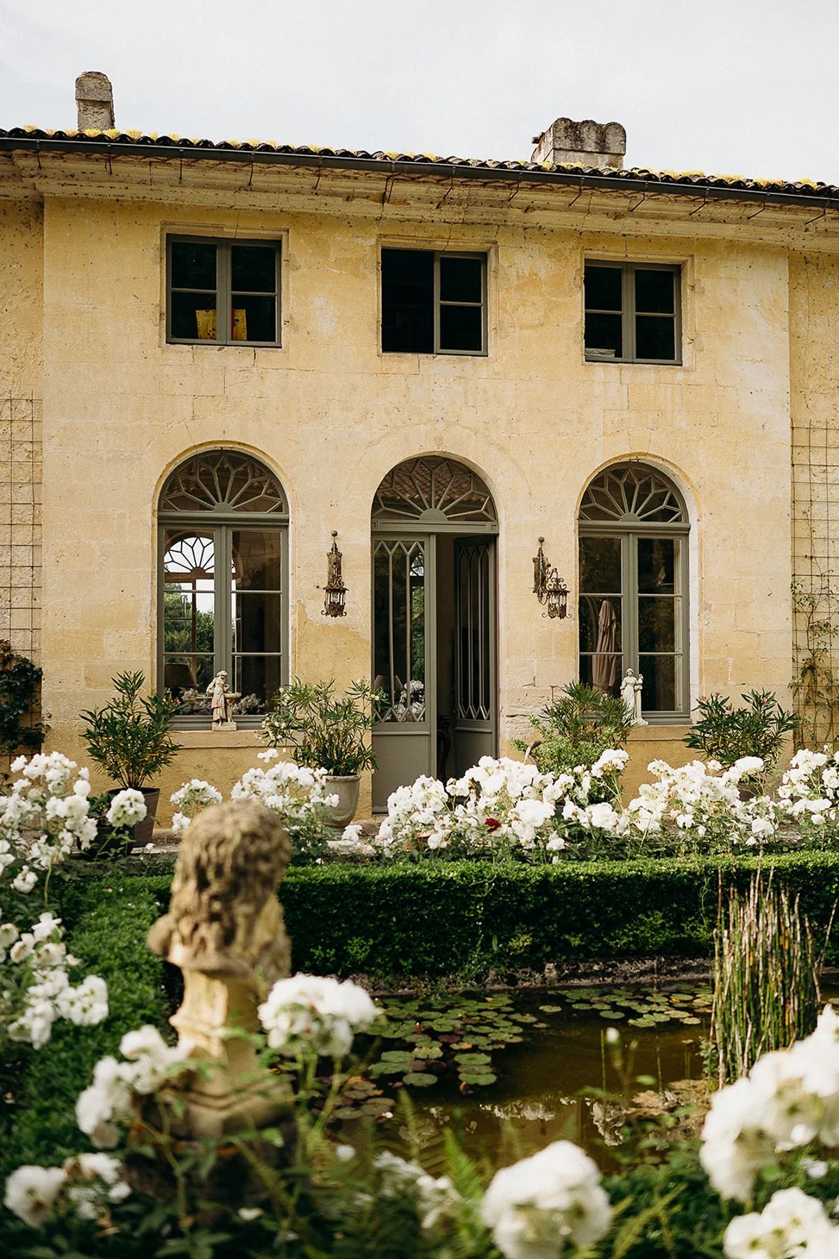 The stone facade with three arched windows, seen across white roses and a lily pond