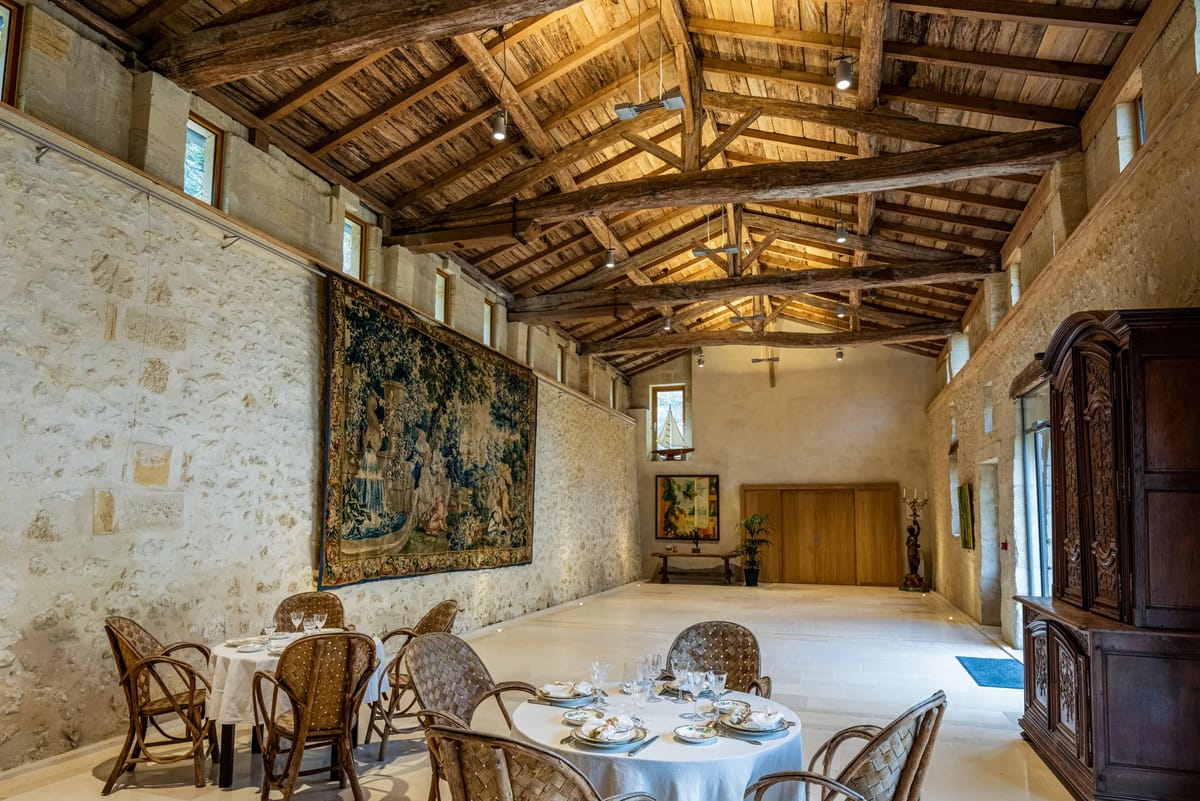 The Galerie Cédrus, a stone hall with exposed timber roof trusses, a large tapestry and set round tables