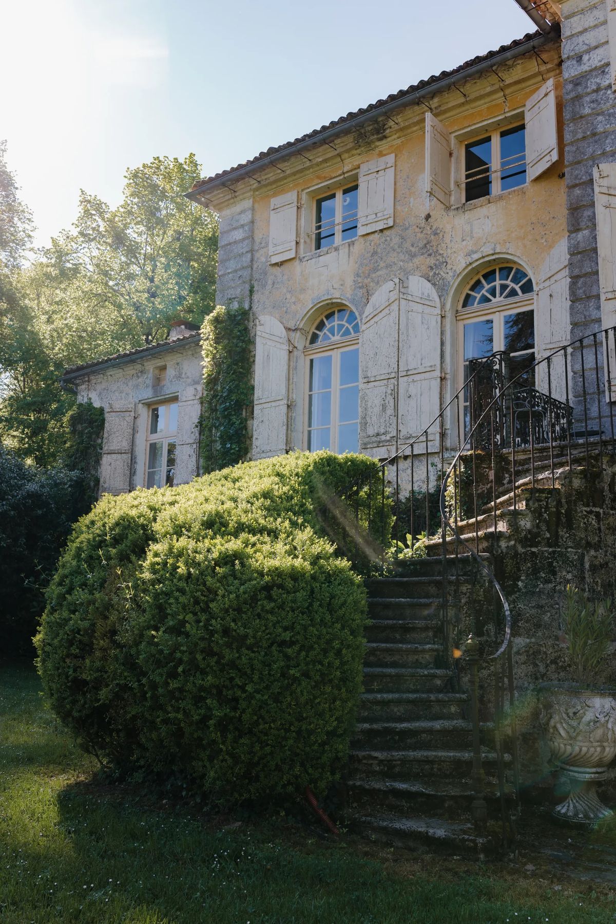 Stone steps rising past a clipped shrub to the shuttered rear facade