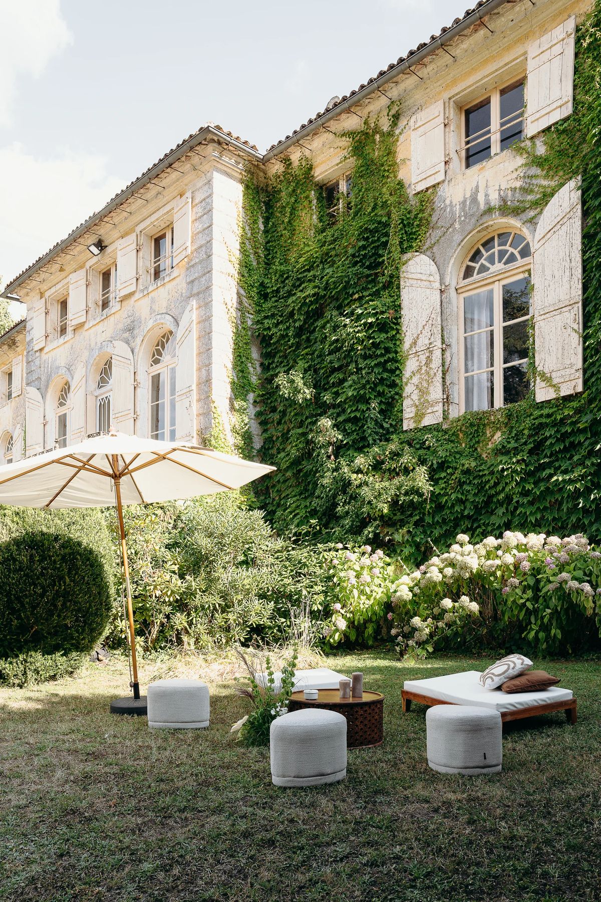 An ivy-covered stone facade with a parasol and low lounge seating on the lawn