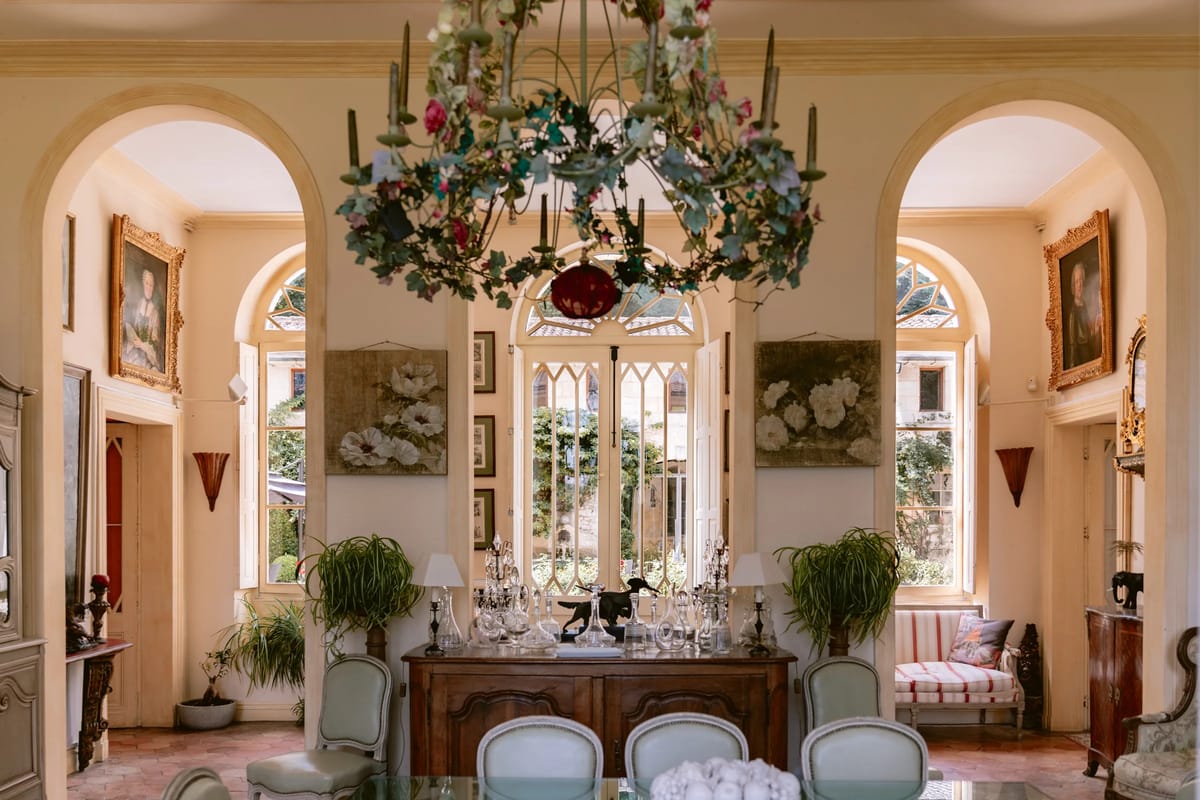 A dining salon with a floral chandelier and a sideboard between arched windows