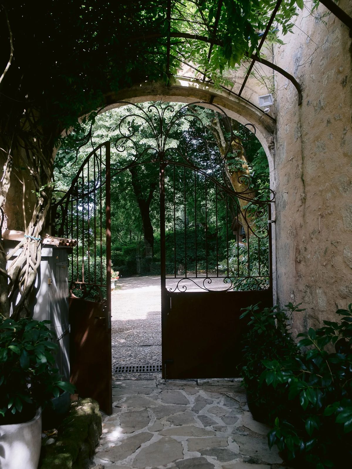 Arched stone gateway with an ironwork gate opening onto a planted path