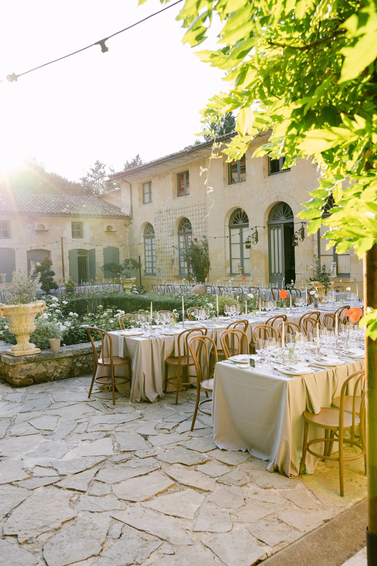 Long tables dressed in beige linen on a stone terrace, with string lights above