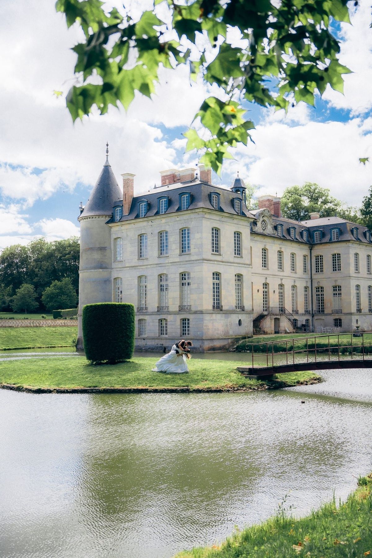 A groom dipping the bride for a kiss on the island in the moat, the château and its round tower behind