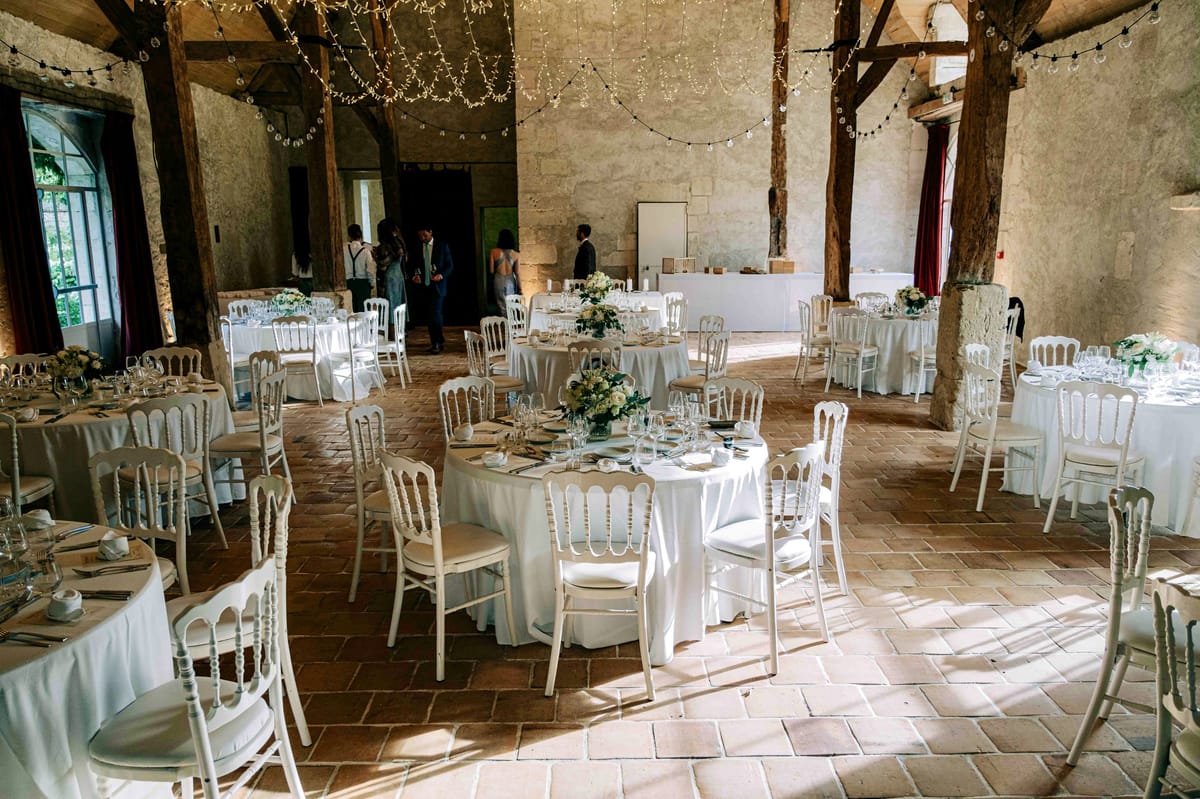 The barn set with round tables and white chairs under strands of fairy lights, a few guests talking by the door