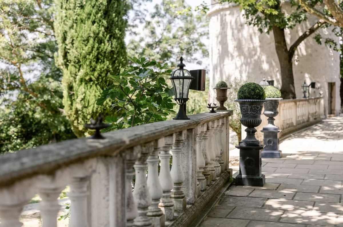 Stone balustraded terrace with clipped topiary in urns leading to the round tower at Le Mas des Cinq Fontaines.