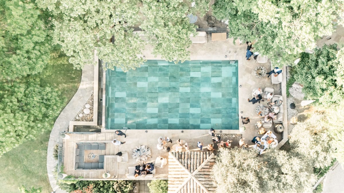 Aerial view of the swimming pool and shaded terrace at Le Mas des Cinq Fontaines with guests gathered poolside under the trees.