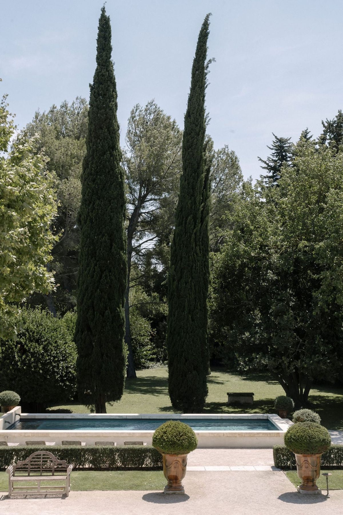 Mas D'Arvieux swimming pool framed by tall cypress trees and garden benches