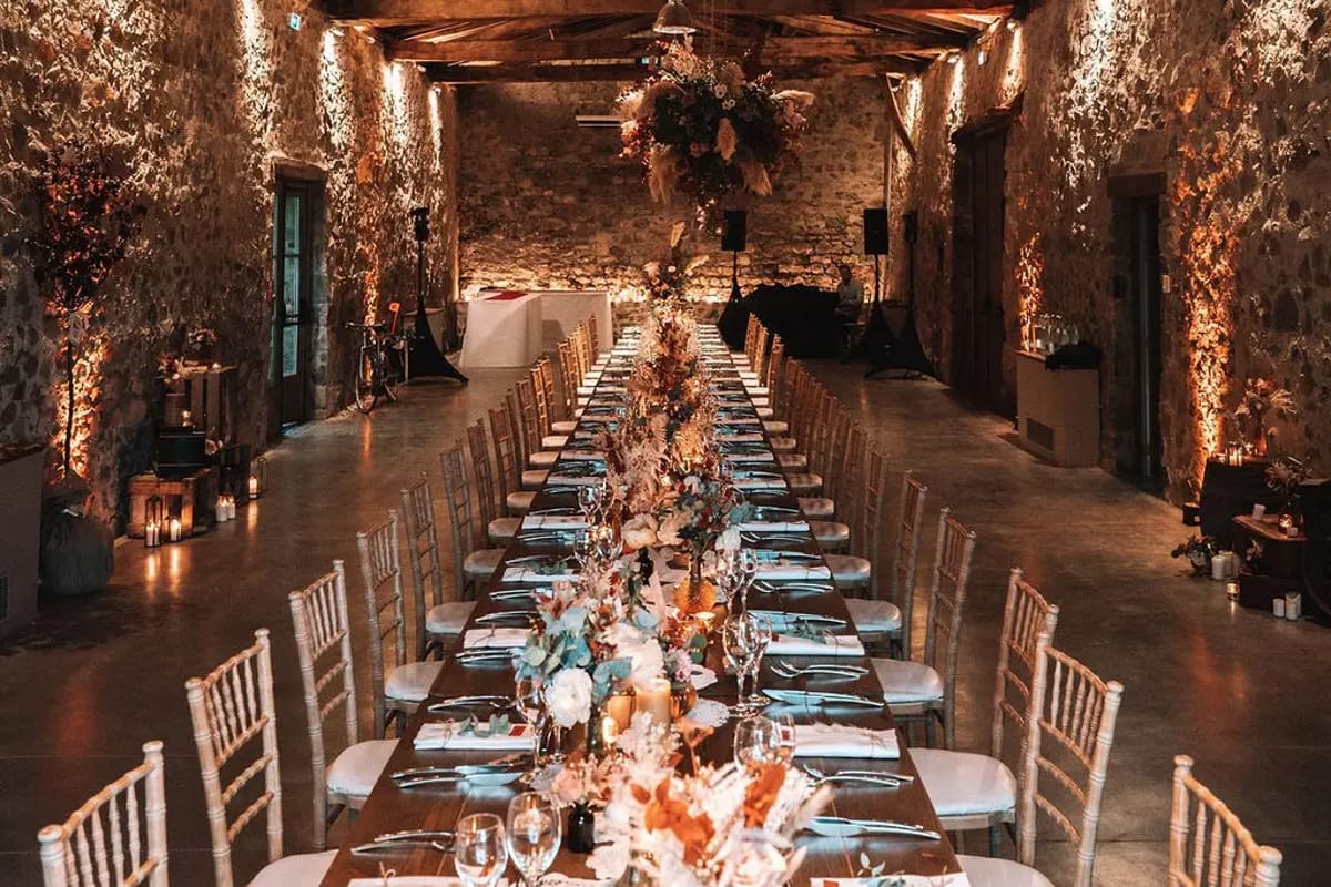 Evening wedding dinner on long tables in the stone barn at Domaine de Vavril, lit by candles and festoon lights
