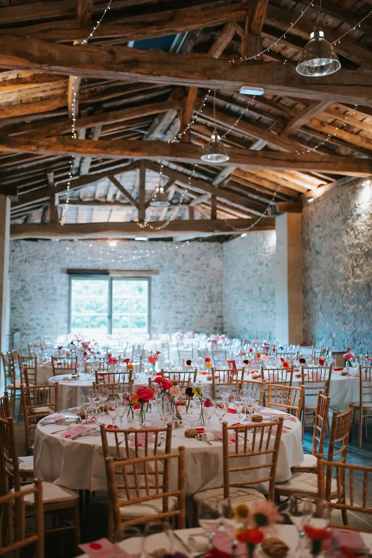 Round tables dressed for a wedding in the beamed stone barn at Domaine de Vavril