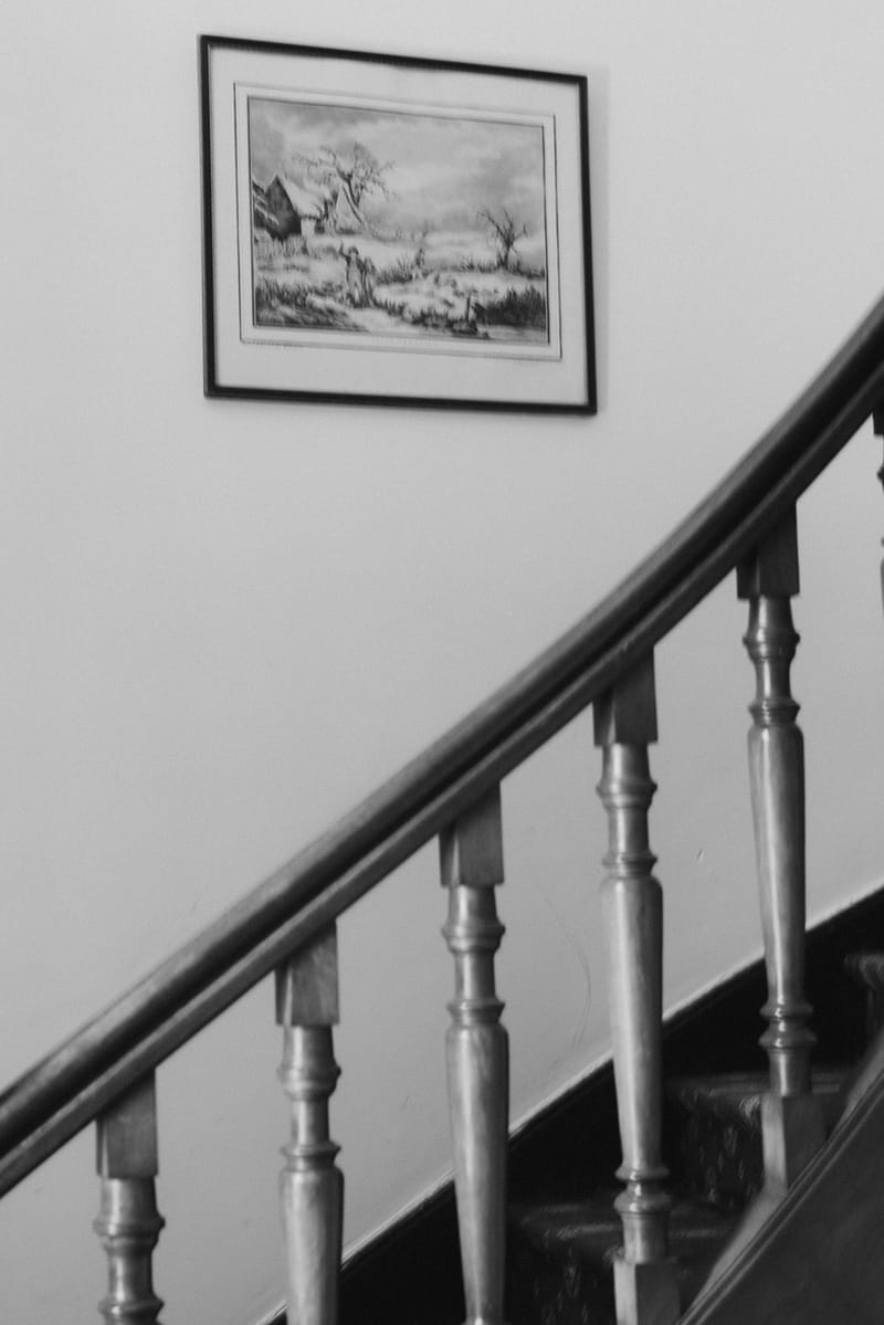 Curved wooden staircase with turned spindle balusters and framed winter landscape print on white wall