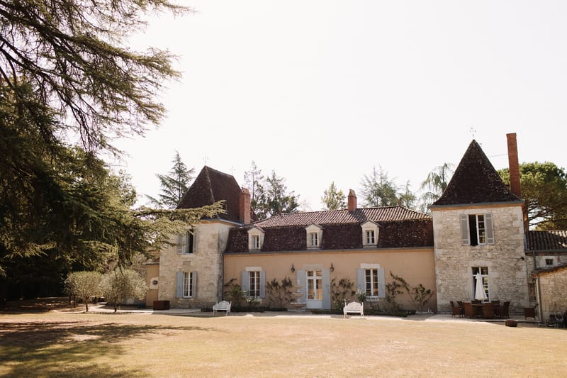 French chateau with twin turrets, terracotta roof, blue-grey shutters, and gravel courtyard with garden benches