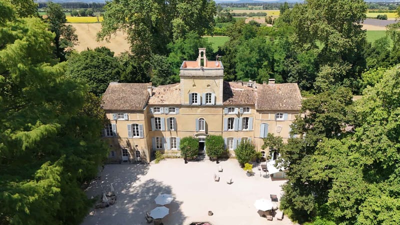 Aerial drone view of Provencal chateau with honey-yellow walls, gravel courtyard, and lavender fields beyond