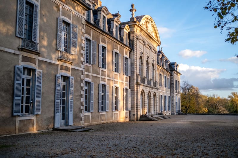 French chateau facade at golden hour with mansard roof dormer windows grey shutters and gravel forecourt
