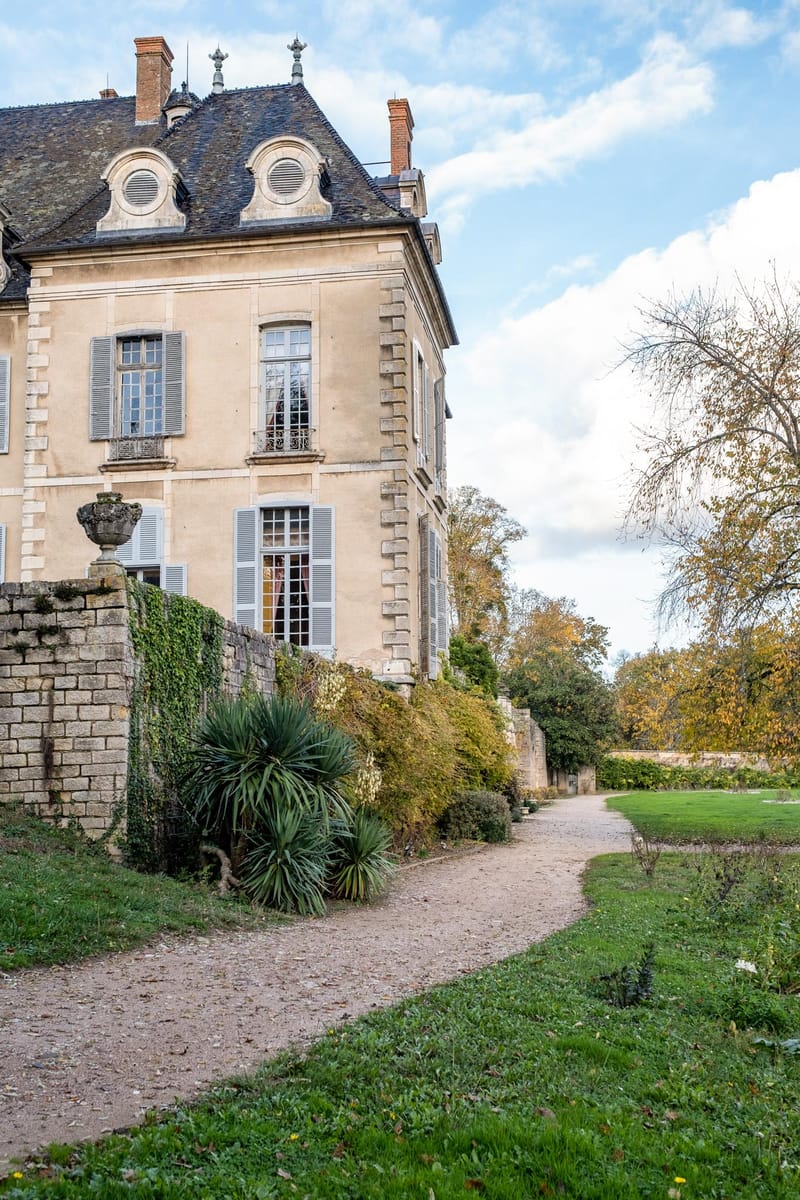 Classical chateau corner facade with beige stone, slate mansard roof, and walled garden path