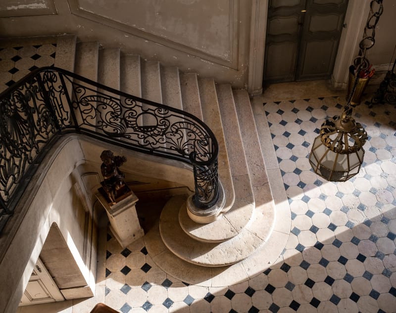 Grand chateau entrance with curved stone staircase, wrought-iron scrollwork, and octagonal tile floor