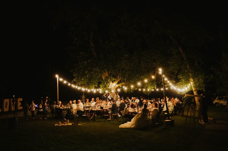 Evening garden reception with sixty guests under festoon lights illuminated LOVE sign and folding chairs