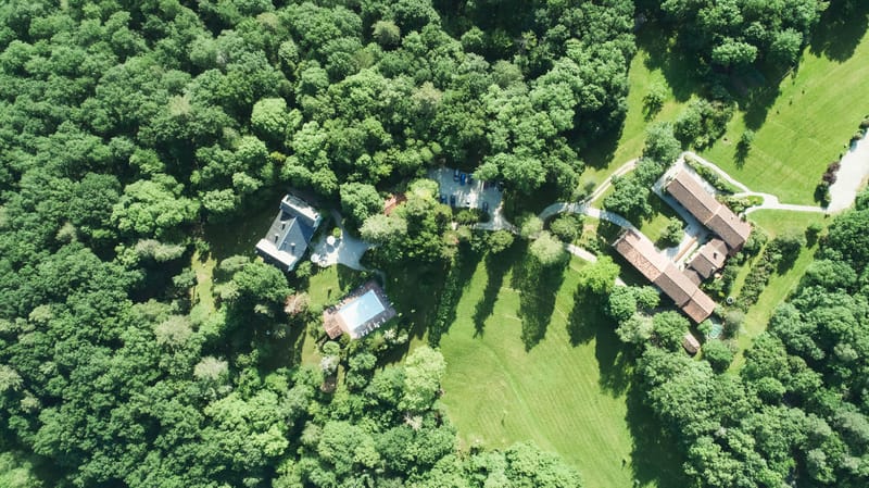 Aerial drone shot of French country estate with manor house, swimming pool, outbuildings, and wooded grounds