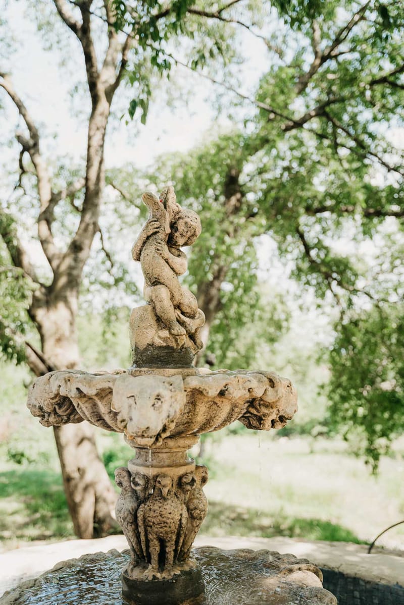 Weathered stone garden fountain with cherub figurine scalloped basin and carved animal pedestal in estate garden