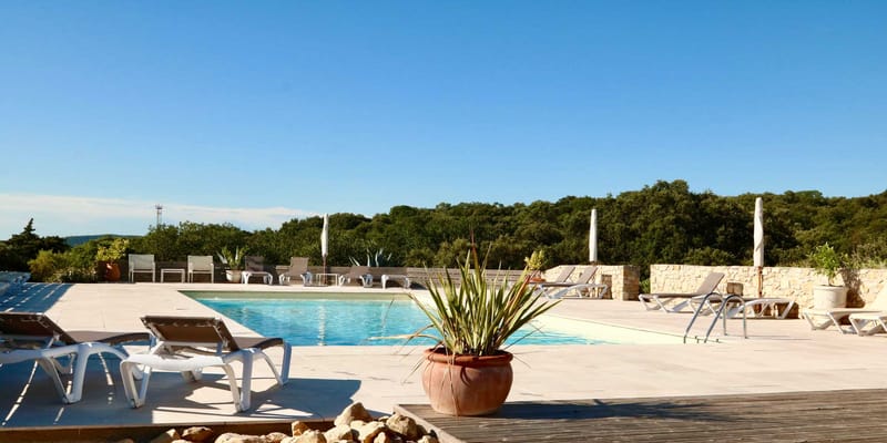 Rectangular pool with loungers white parasols terracotta planter and dry-stone wall at French countryside venue