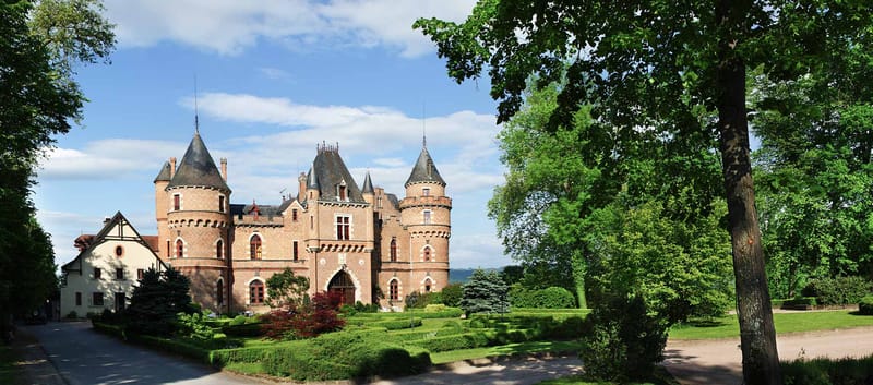 Wide exterior of pink-red brick French chateau with conical turret towers and formal hedgerow gardens