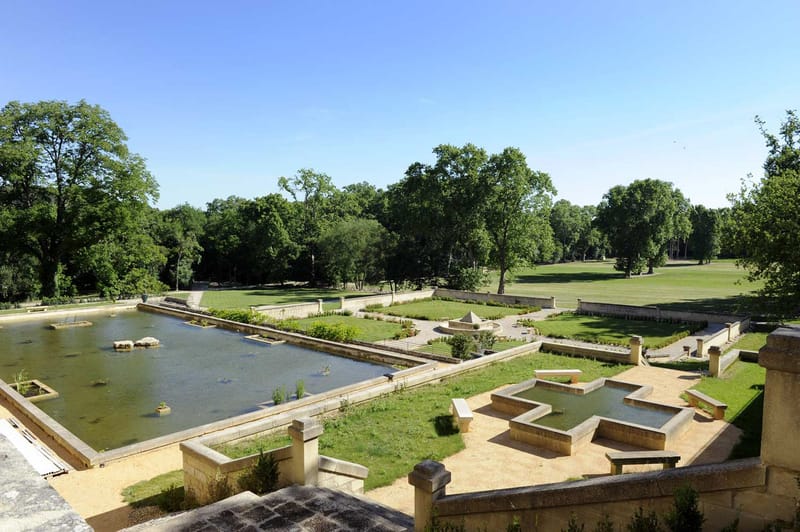 Elevated view of formal chateau grounds with limestone reflecting pool, terraced gardens, and mature trees
