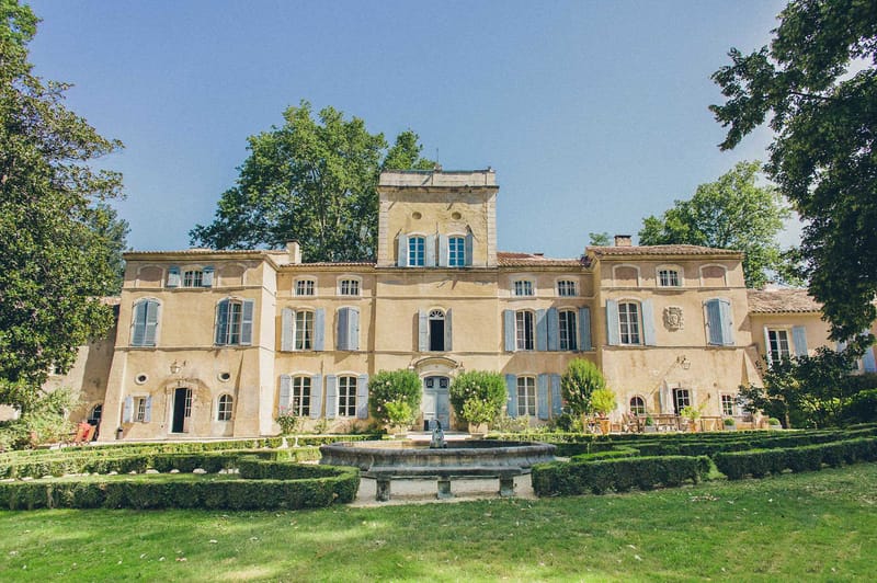 Ochre-yellow Provencal chateau with blue shutters and formal parterre gardens with stone fountain