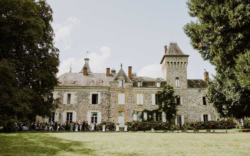 Fifty guests mingling on chateau terrace with white cocktail tables turreted stone building and pink flowering shrubs