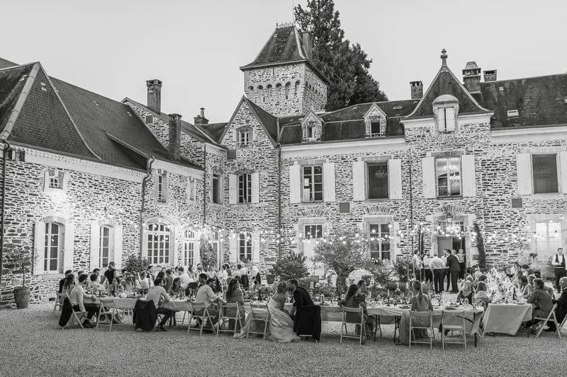 Black and white elevated view of chateau courtyard reception with 60-80 guests under string lights at evening