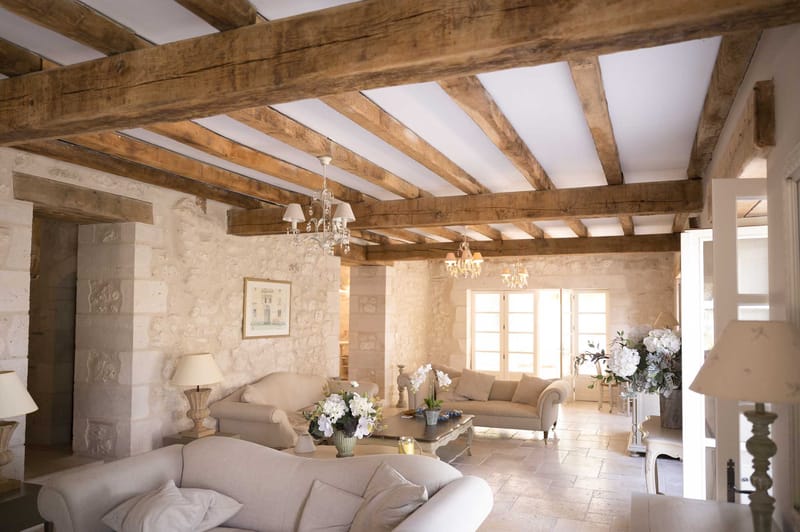 French country salon with exposed beams, cream linen sofas, crystal chandeliers, and white hydrangea arrangements