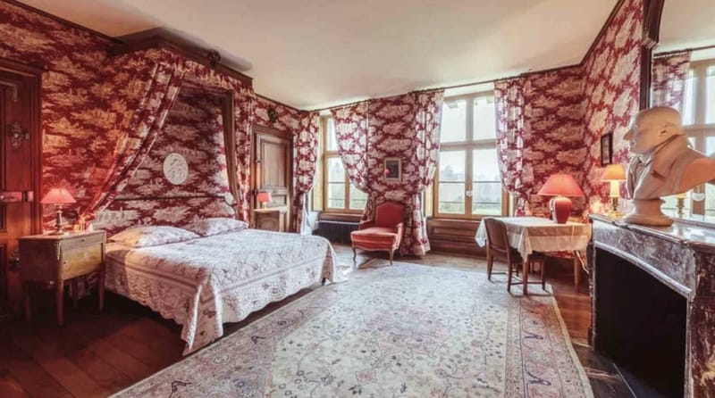 Chateau bedroom suite with crimson toile de Jouy wallpaper four-poster canopy bed and marble fireplace