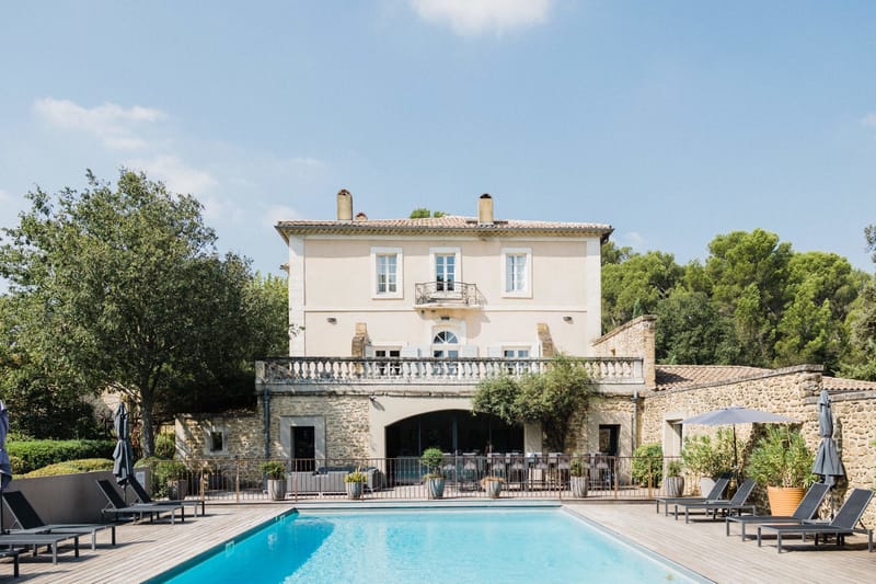 French bastide with cream facades, pool terrace, sun loungers, and arched passageway connecting buildings