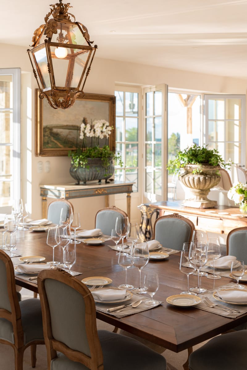 French country dining room with walnut table, Louis XV blue chairs, gilt lantern, and French doors to terrace