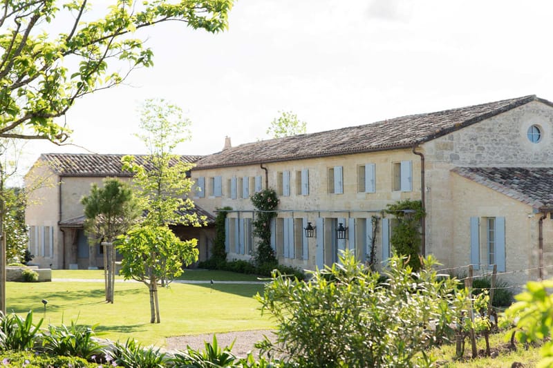 Golden limestone French country estate with terracotta roof, blue shutters, and manicured lawn