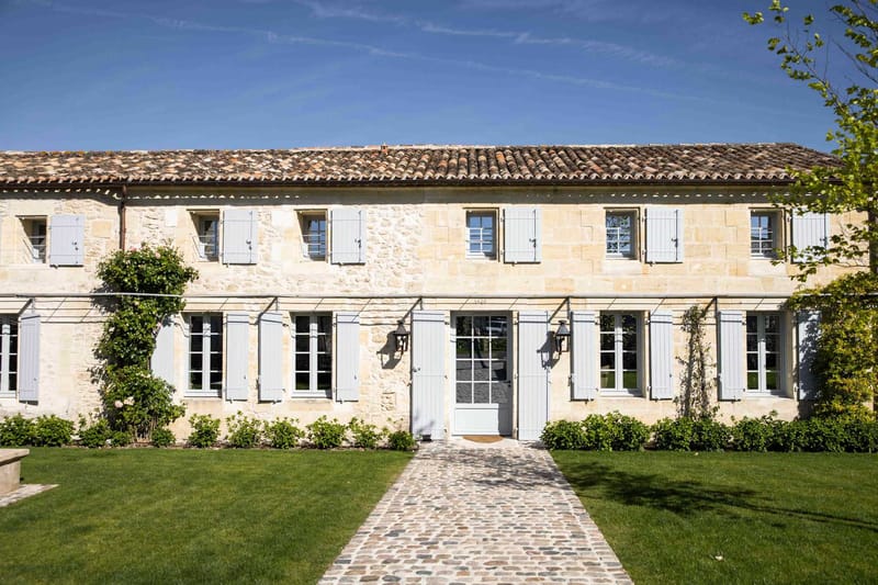 Pale limestone French country manor with blue-grey shutters, cobblestone path, and climbing roses
